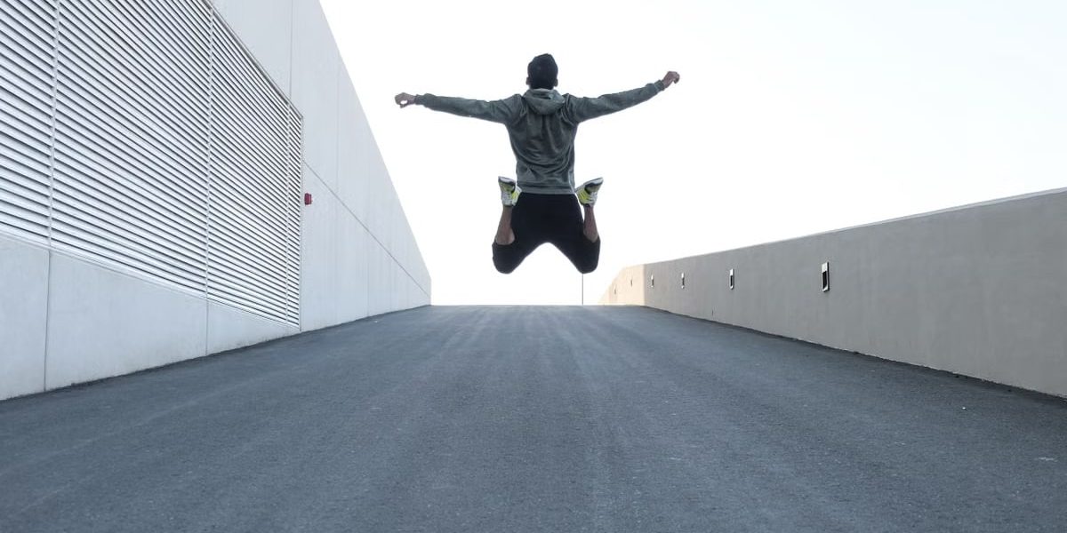 Man jumping on urban road with arms spread wide in Dubai, showcasing freedom and energy.