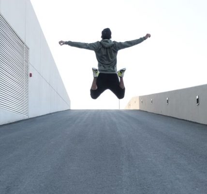 Man jumping on urban road with arms spread wide in Dubai, showcasing freedom and energy.